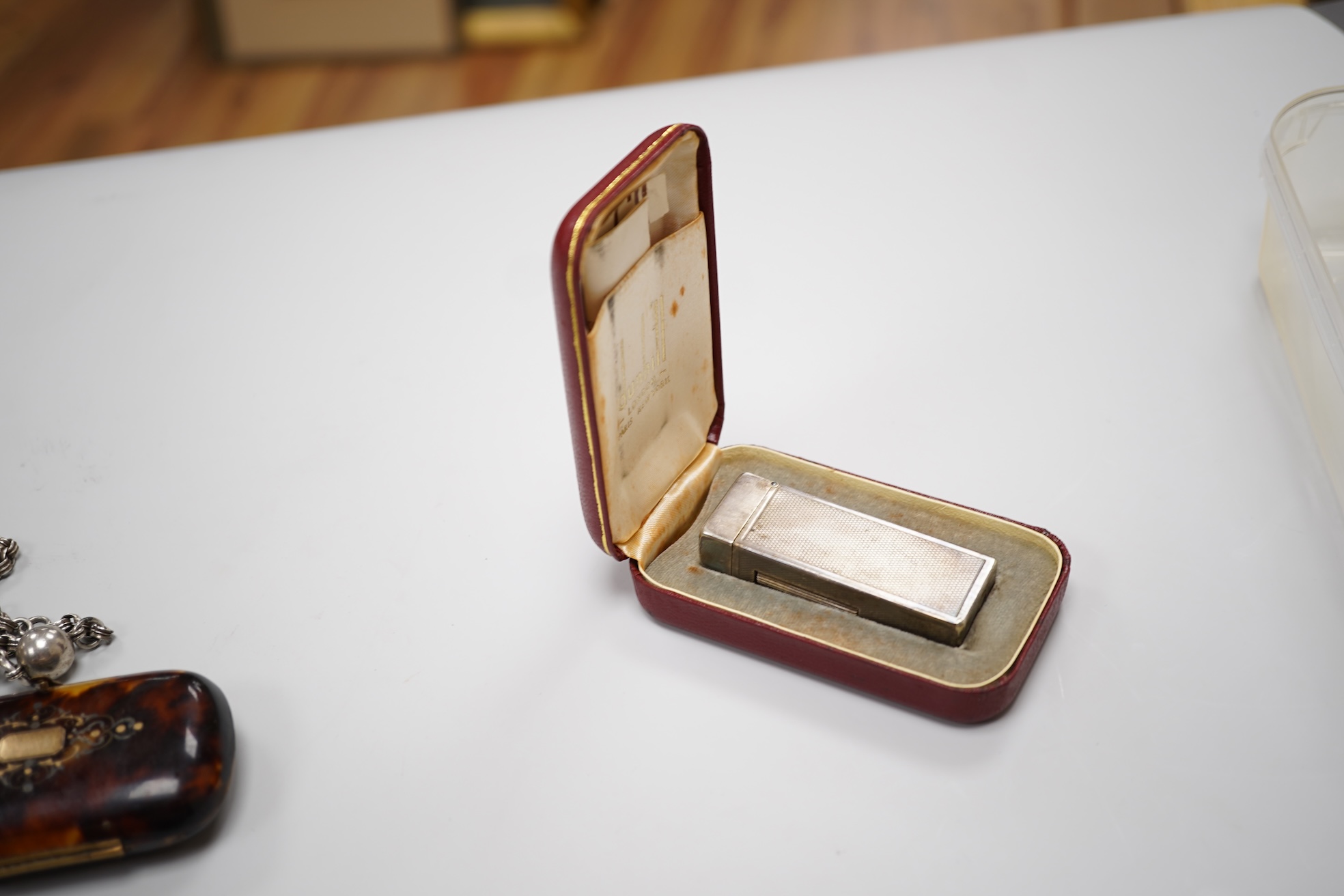 An early 20th century white metal oval locket, 40mm, on a silver chain, a silver plated Dunhill lighter, in Dunhill box, a white metal cased manual wind wrist watch and a tortoiseshell purse.